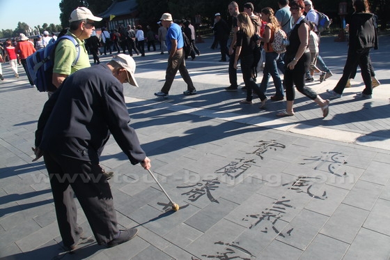 An old man writing chinese calligraphy with a big brush dipped in water