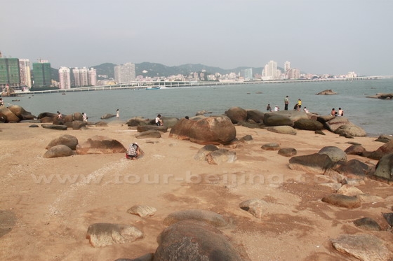 People are playing on the rocks and beaches with the cityscape as the backdrop.