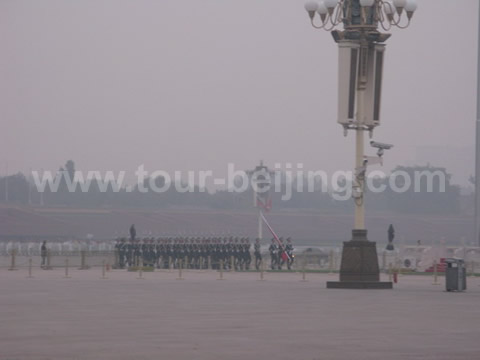 A procession of soldiers carrying the flag emerging from Tiananmen Tower marching toward the flag pole.